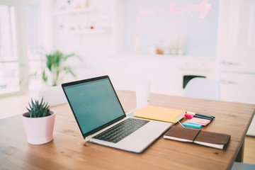 Opened laptop with white screen and notebooks on wooden table