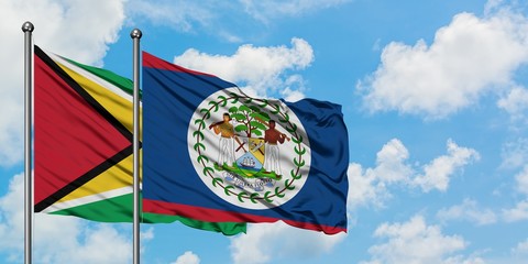 Guyana and Belize flag waving in the wind against white cloudy blue sky together. Diplomacy...