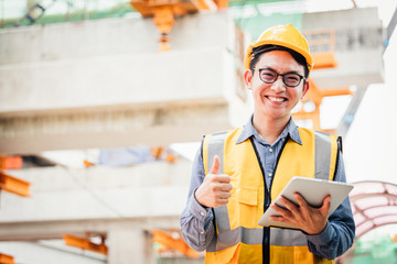 Image outside the industrial construction engineers in yellow protective helmet discuss new project while using laptop and happy smile on the open building site near the crane.