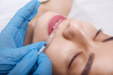 Obraz na płótnie Canvas Facial Beauty Injections. Portrait Beautiful Young Woman Receiving Hyaluronic Acid Injection. Closeup Of Hands In Gloves Holding Syringe Near Attractive Female Face.