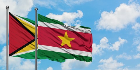 Guyana and Suriname flag waving in the wind against white cloudy blue sky together. Diplomacy concept, international relations.