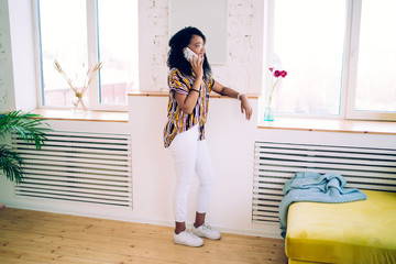 Cheerful black woman speaking on phone while standing in living room