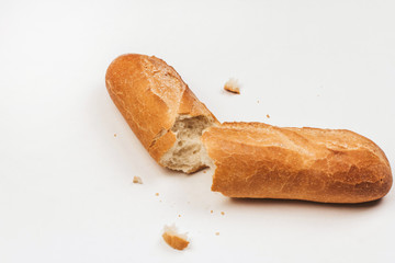  Two halves of a broken crispy baguette and bread crumbs on a white background.