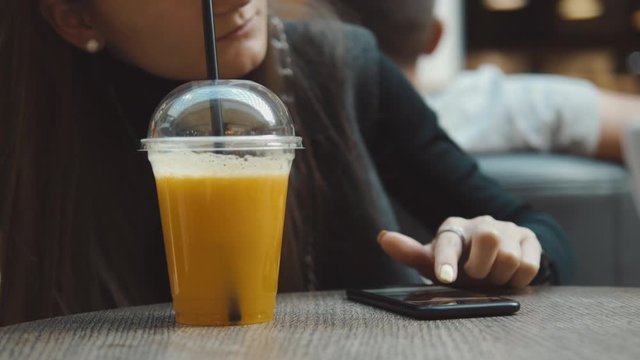 Young woman browsing on smartphone in cafe on wooden table, drinking juce. Businesswoman typing on mobile phone. 4K UHD