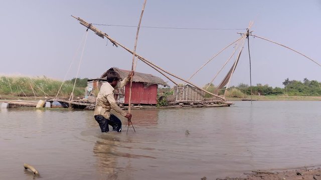 Clammer is digging for clams into the river-bottom by the riverside. Chinese fishing net  as backdrop