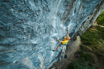 top view of man rock climber in yellow t-shirt, climbing on a cliff, searching, reaching and...