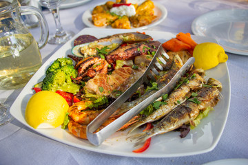 Fototapeta na wymiar Big plate with seafood, sepia, fish, shrimps, mussels served with retsina, in taverna in Greece