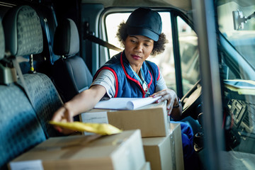 African American courier sorting packages for delivery while sitting in a van.
