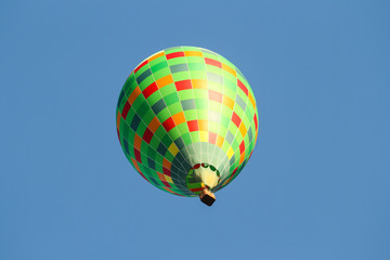 Fototapeta premium Green hot air balloon flying over the small city in a clear blue sky.