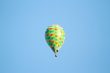 Green hot air balloon flying over the small city in a clear blue sky.