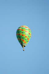 Green hot air balloon flying over the small city in a clear blue sky.