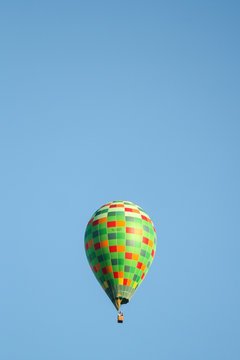 Green hot air balloon flying over the small city in a clear blue sky.