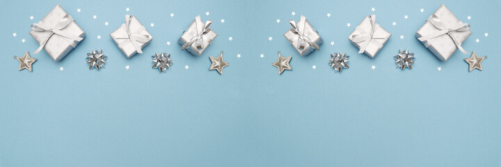 Gifts or present boxes in silver with silver bows and tree ball ornaments and little silver stars, table tob view. Composition for Christmas. Blue pastel background.