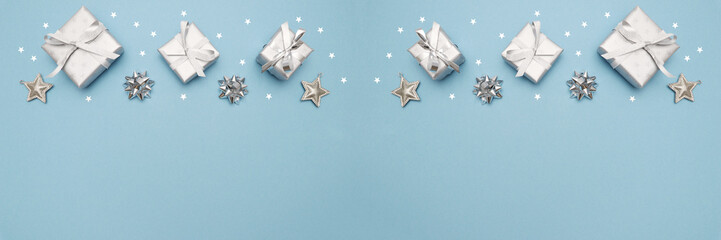 Gifts or present boxes in silver with silver bows and tree ball ornaments and little silver stars, table tob view. Composition for Christmas. Blue pastel background.