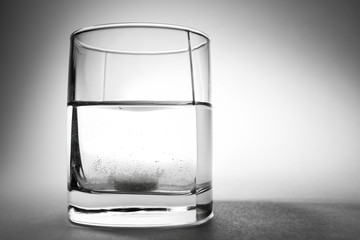 An effervescent tablet dissolves in a glass of water on a gray background.
