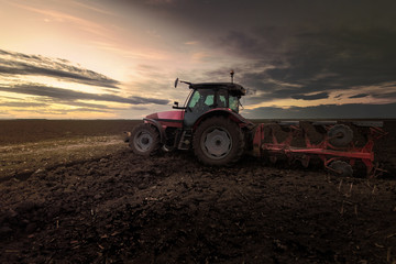 Fototapeta premium Ciągnik orze pola o zachodzie słońca