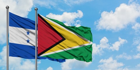 Honduras and Guyana flag waving in the wind against white cloudy blue sky together. Diplomacy concept, international relations.