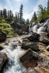 Alpine waterfall in mountain forest under blue sky.