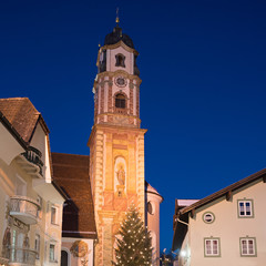 Fototapeta na wymiar St. Peter und Paul Kirche in Mittenwald zur Weihnachtszeit, beleuchtet in der Dämmerung, mit Christbaum