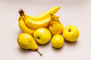 Assorted bright yellow fruits. Fresh banana, pear, apple, lemon. Harvest on a stone background