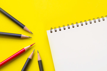 Red color pencil , black pencils and notebook on yellow background 