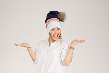 Portrait of happy young smiling woman wearing many colorful knitted hats over white background. Spreads her arms to the side and is surprised. Empty space for text.