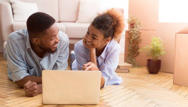 Afro Couple Using Laptop Lying On Floor In New House
