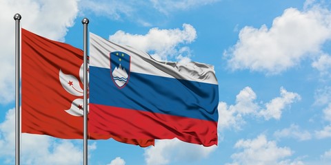 Hong Kong and Slovenia flag waving in the wind against white cloudy blue sky together. Diplomacy...