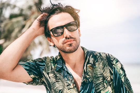 Stylish Sexy Young Brunette Man With A Beard In A Hawaiian Shirt, Portrait On A Tropical Beach