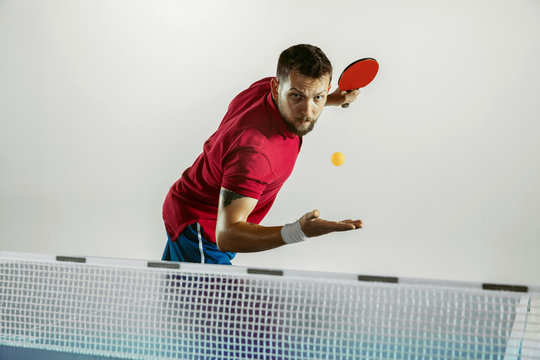 Power. Young man plays table tennis on white studio background. Model plays ping pong. Concept of leisure activity, sport, human emotions in gameplay, healthy lifestyle, motion, action, movement.