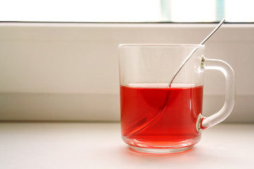 glass cup into spoon with red fruit tea standing on white windowsill