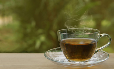 A glass cup of  hot tea and vapour on wooden table with natural background, selective focus