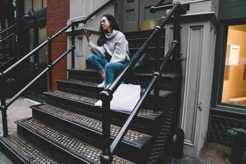 Young woman sitting on stair surfing mobile on street