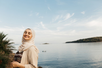 portrait of young European Muslim women with hijab and looking at the camera. Sea is in the background. She is happy and relaxed.