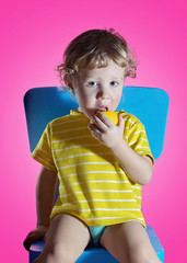 Naklejka premium Cute little boy in yellow jacket with lemon in hand, pink wall on background. Close up studio portrait of boy.