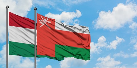 Hungary and Oman flag waving in the wind against white cloudy blue sky together. Diplomacy concept, international relations.