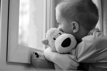 Sad boy at the window and bear toy, black and white image