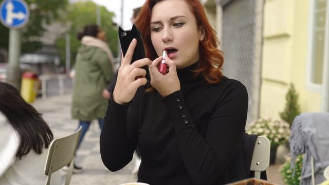 Redhead woman in an outdoor cafe during breakfast wearing red lipstick and black sweater - Doing makeup and getting ready