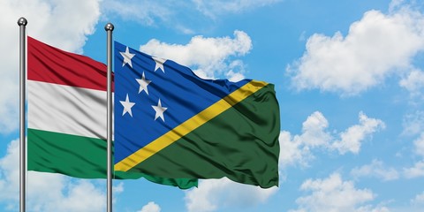 Hungary and Solomon Islands flag waving in the wind against white cloudy blue sky together. Diplomacy concept, international relations.