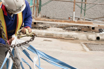 Workers wear white hats, blue jackets and reflective clothing, fastening the strap to the crane's...