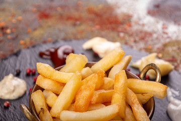 Vintage cooper bowl of french fries chips potato and sauces on black stone slate over rusty background. top view