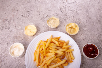 White plate of french fries chips potato and sauces on gry concrete background. top view. copy spacce