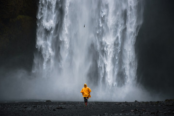 Tourist wearing a yellow raincoat walks from the Skogafoss waterfall in Iceland