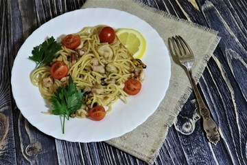 Seafood pasta, cherry, parsley, lemon slice on a plate.