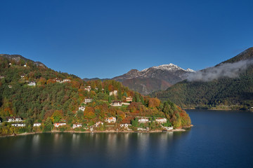 Fototapeta premium Panoramic view of the mountains and lake Pieve di Ledro, Italy. Autumn season, the reflection in the water of the mountains, trees, blue sky