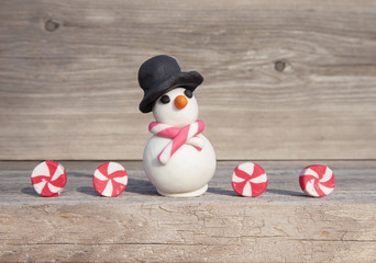 Playful Christmas concept. Handmade miniature snowman with candies, in front of soft wood background. 