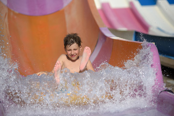 Boy having fun on the water slide on floater in the aqua fun park. He is enjoying his summer...