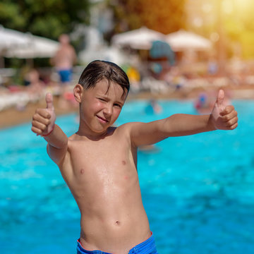 Portrait of Caucasian boy in swimming pool at resort. He is smiling, making like gestures and looking into camera.