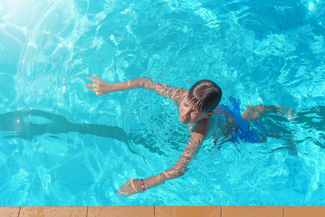 Learning to swim. Boy swimming along the side of pool.