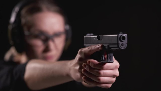 Young Blonde Female Aiming a Hand Gun in a Shooting Range with Ear and Eye Protection on in Slow Motion
